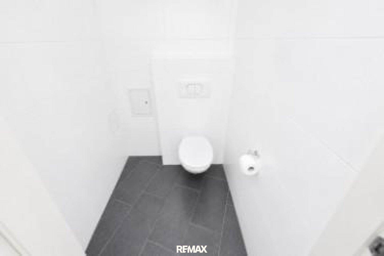 Sauberes Gäste-WC mit wandhängender Toilette und dunklem Fliesenboden, in gutem Zustand.