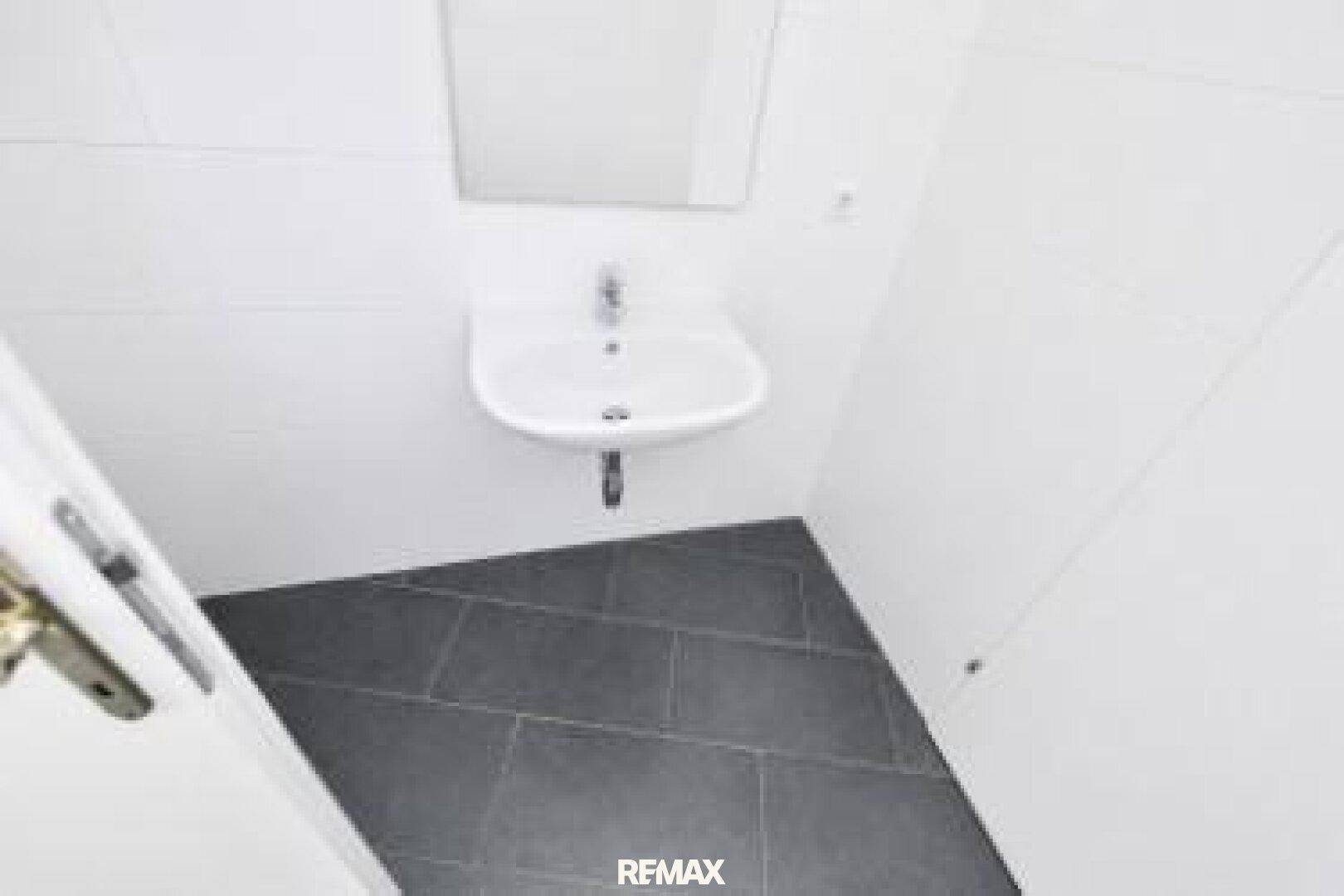 Modernes Gäste-WC mit weißem Waschbecken und dunklen Fliesen auf dem Boden, in gepflegtem Zustand.