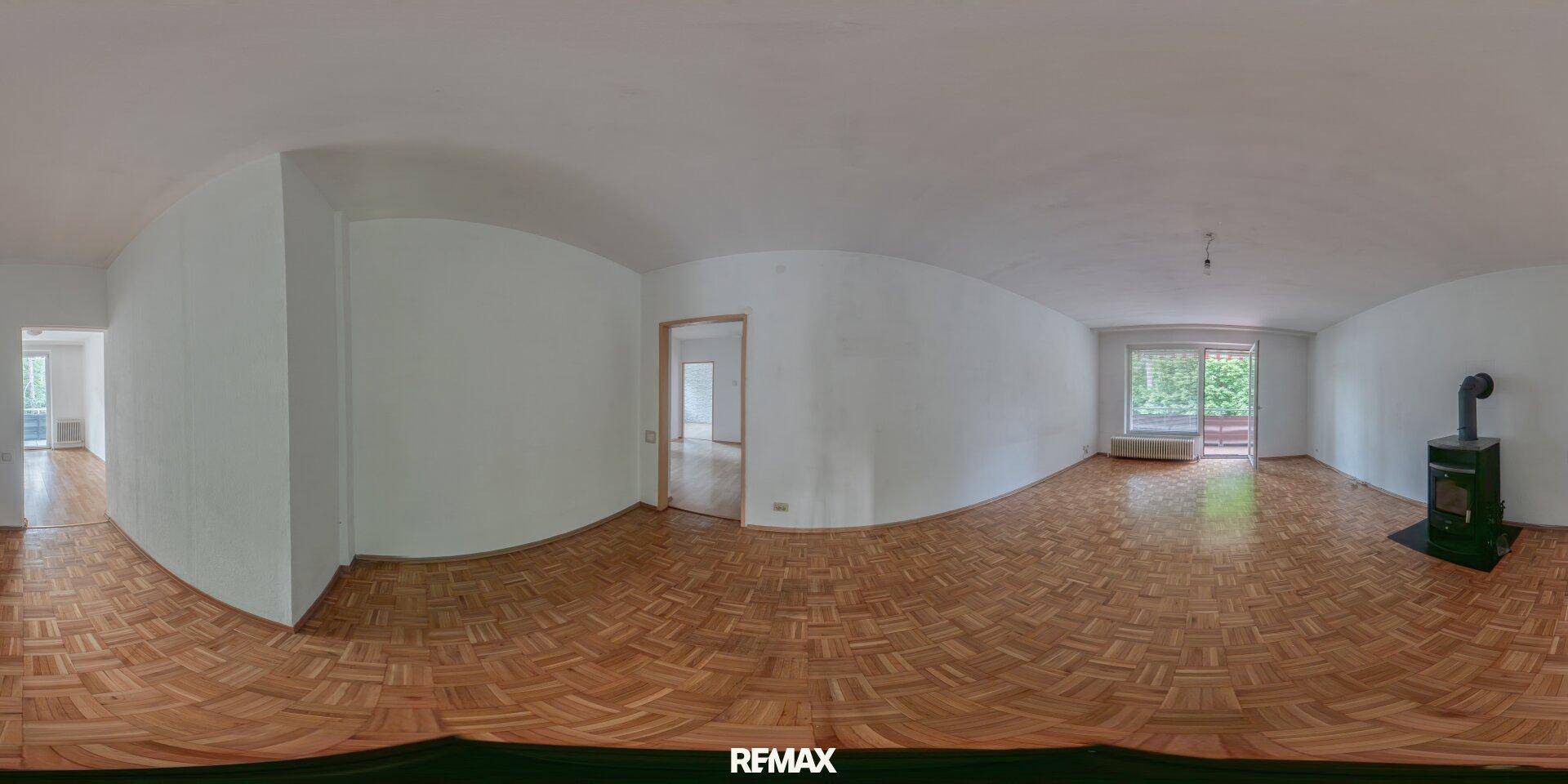 Panoramaansicht eines leeren Wohnzimmers mit Parkettboden, Kaminofen und Balkonzugang.