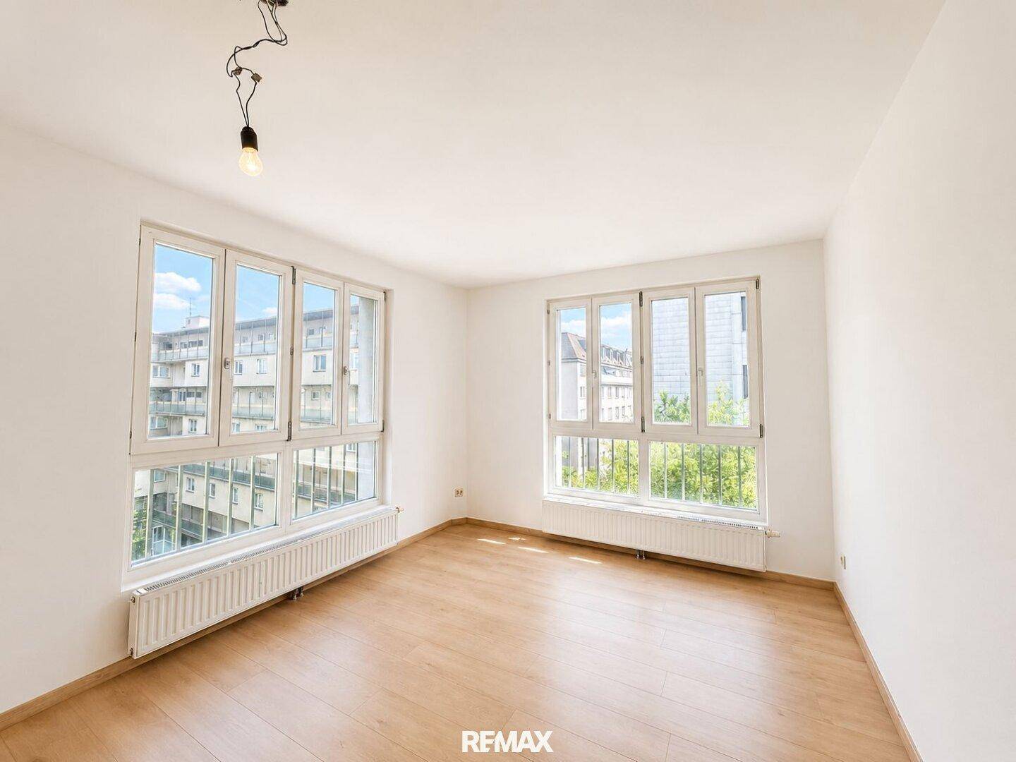 Heller Wohnraum mit großen Fenstern, Holzboden und Blick auf die Stadt.
