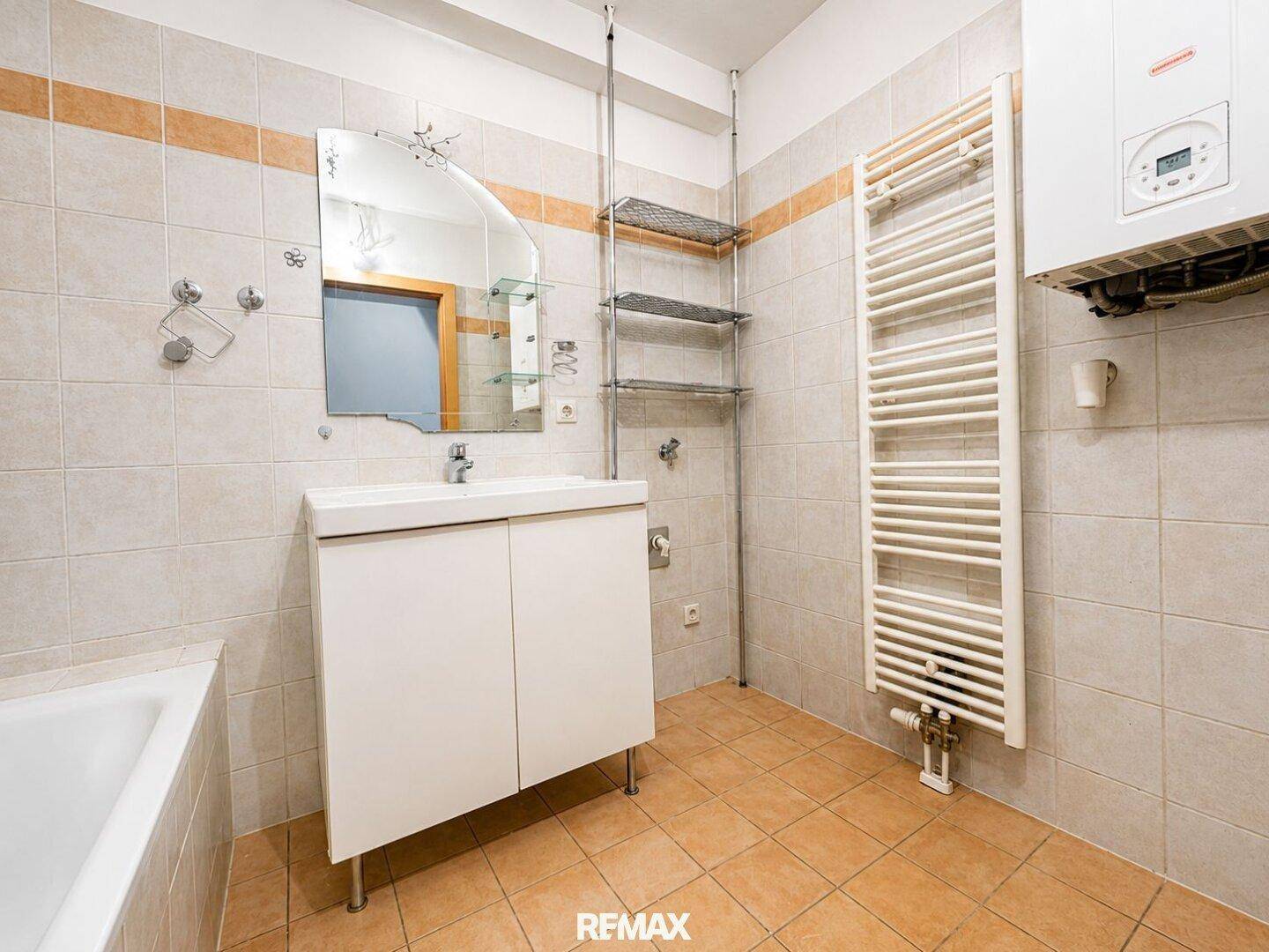 Badezimmer mit Fliesen, Waschtisch, Badewanne und Handtuchheizkörper.