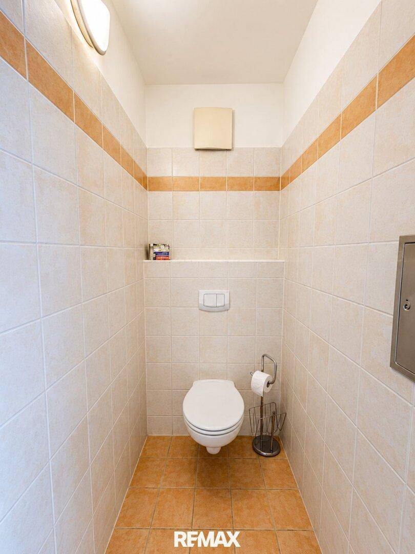 Kleines WC mit Wand-WC, Fliesen und Abluftventilator.