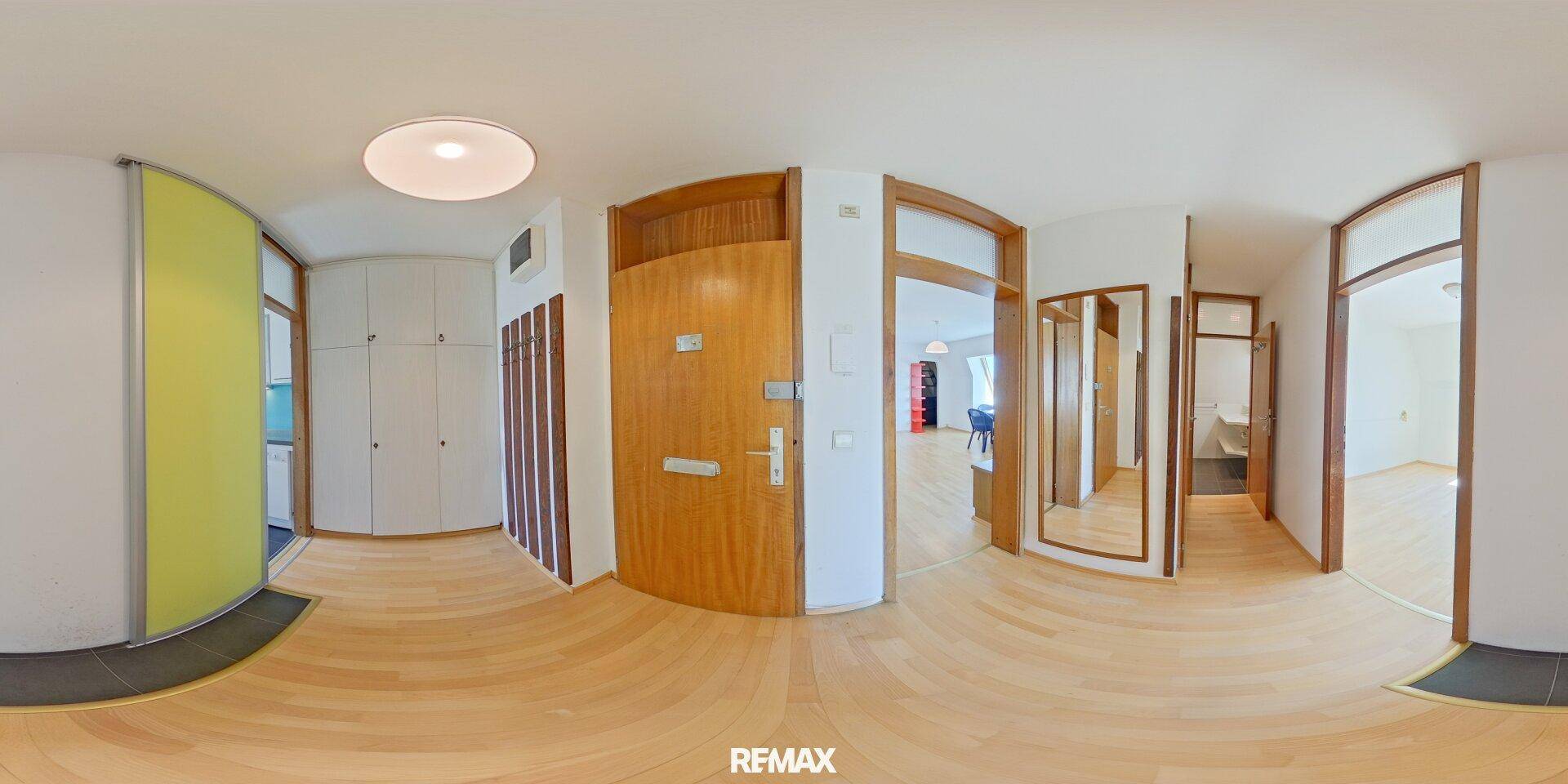 Panoramablick auf den hellen Eingangsbereich mit Holztür, Einbauschränken und Zugang zu weiteren Räumen.