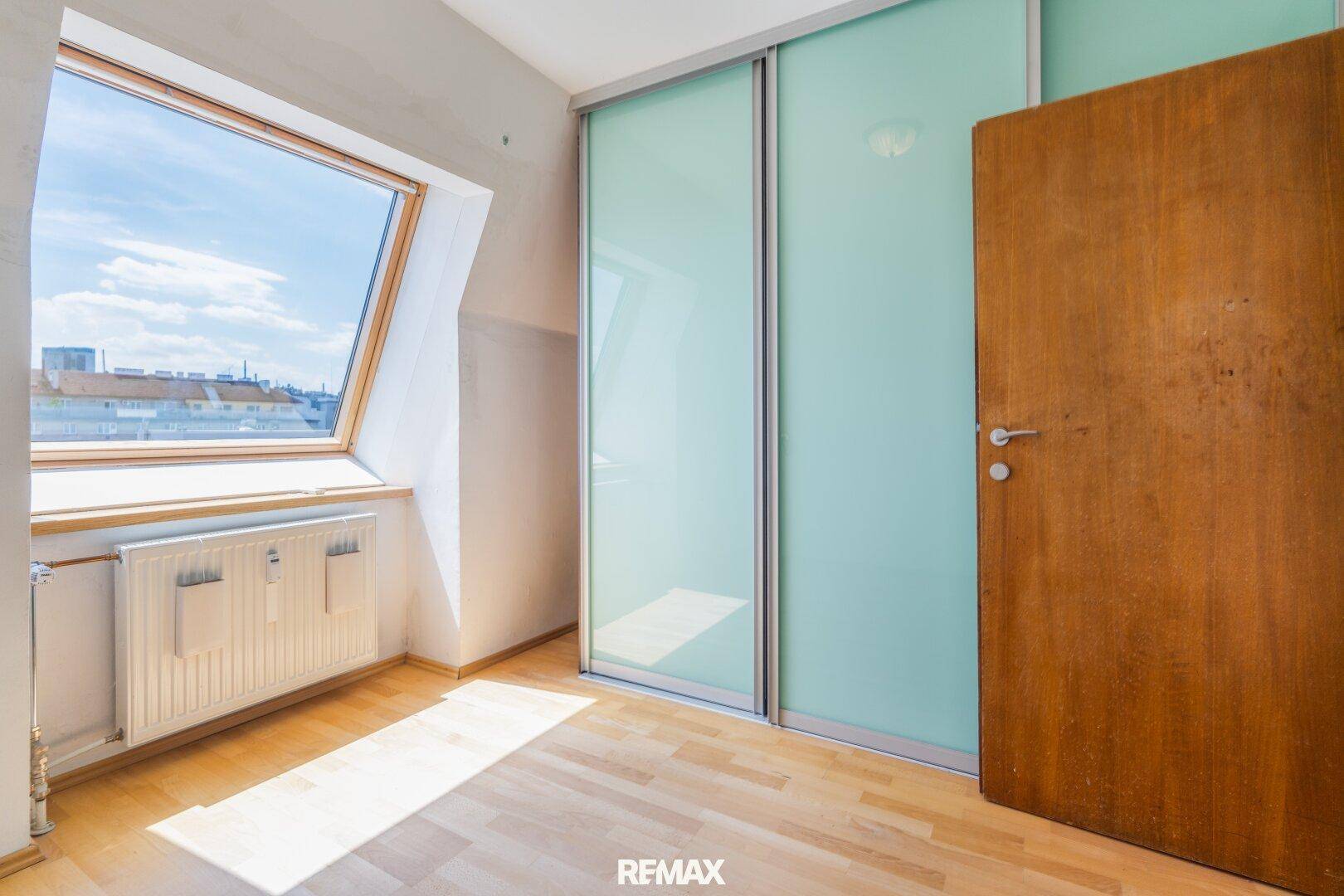 Helles Schlafzimmer mit Holzboden, großem Dachfenster und praktischem Schiebetürenschrank.