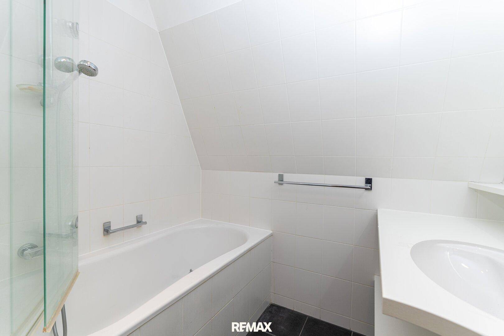 Modernes Badezimmer mit Badewanne, Dusche, Waschbecken und weißen Fliesen unter Dachschräge.