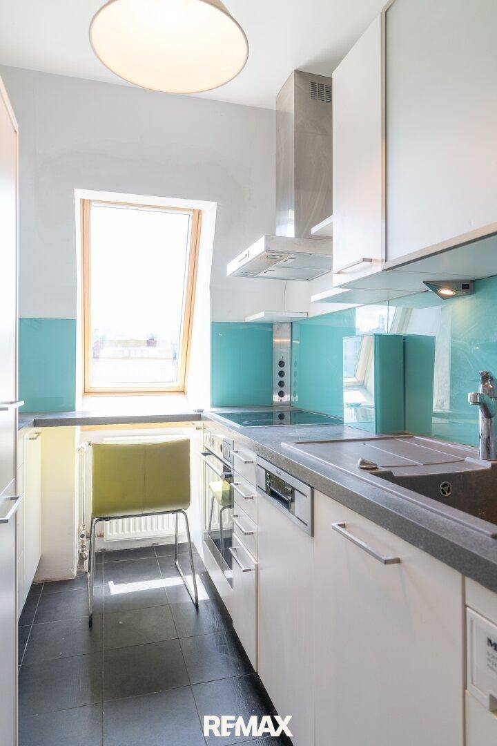 Moderne Küche mit weißen Schränken, türkiser Rückwand, dunklem Fliesenboden und Dachfenster.