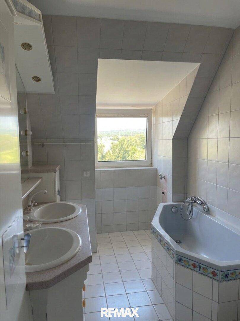 Gefliestes Badezimmer im Dachgeschoss mit Doppelwaschbecken, Eckbadewanne und Fenster.