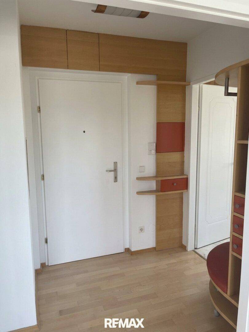 Eingangsbereich mit Holzboden, weißer Tür und integrierten Holzschränken für zusätzlichen Stauraum.