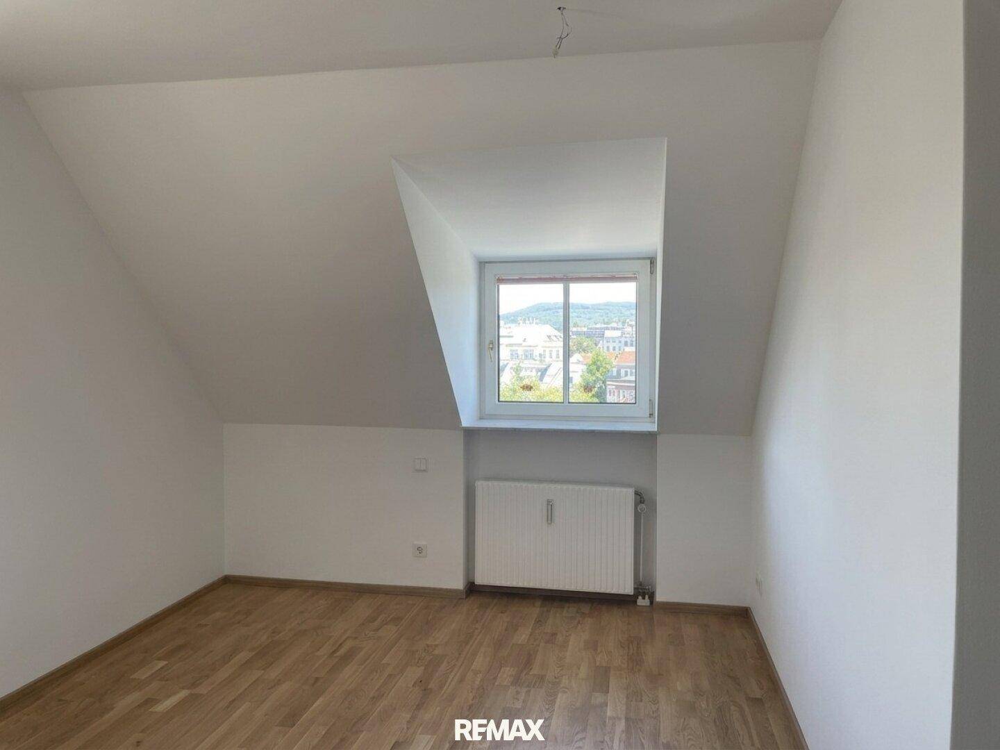 Helles Schlafzimmer im Dachgeschoss mit Holzboden, Dachschräge und Fenster mit Ausblick.
