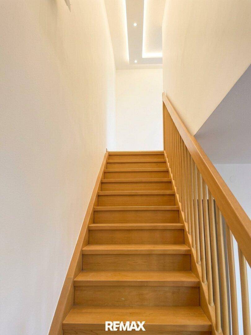 Heller Treppenaufgang mit Holzstufen und weiß gestrichenen Wänden, schlicht und modern.