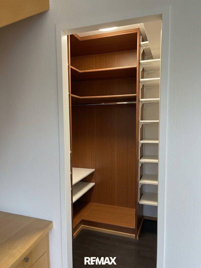 Geräumiger begehbarer Kleiderschrank mit Holzregalen und viel Stauraum, ungenutzt.