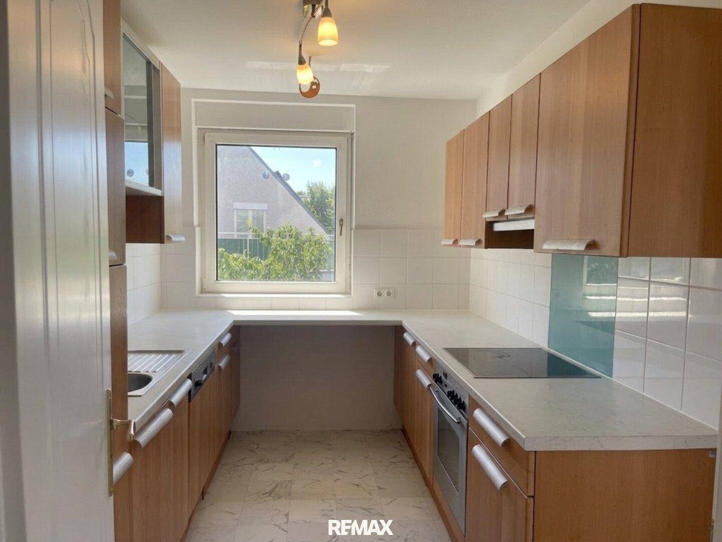 Funktionale Küche mit Holzschränken, weißen Fliesen und Fenster mit Blick ins Grüne.