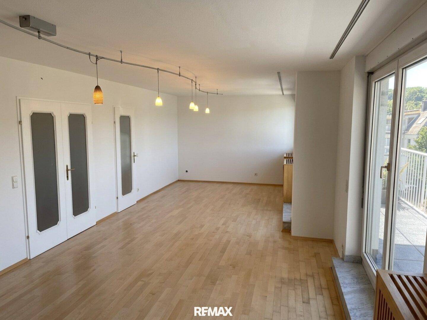 Offener Wohn- und Essbereich mit Holzboden und Zugang zu einem Balkon, unmöbliert.