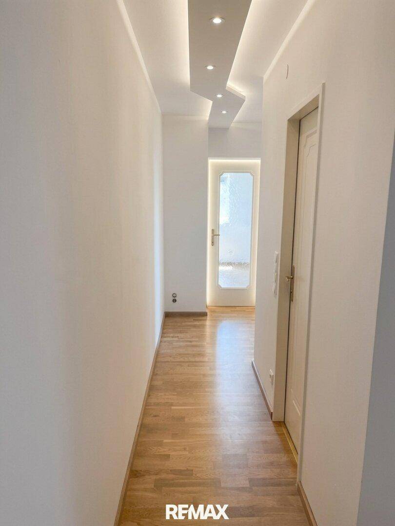 Heller Flur mit Holzfußboden, weißen Wänden und moderner Deckenbeleuchtung.