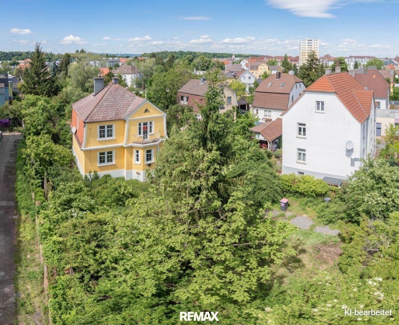 Luftaufnahme eines gelben Hauses mit Satteldach, umgeben von viel Grün und weiteren Wohnhäusern in einer Vorstadtgegend.