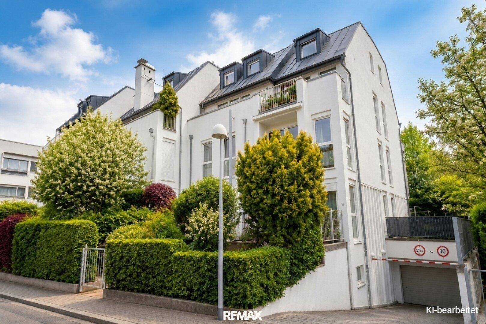 Modernes Mehrfamilienhaus mit weißer Fassade, gepflegter Bepflanzung und Tiefgaragenzufahrt.