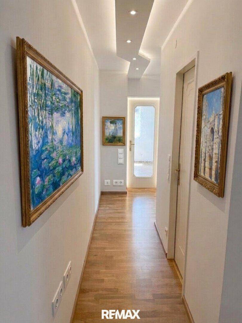 Heller Flur mit Holzfußboden, indirekter Beleuchtung und Kunstwerken an den Wänden.