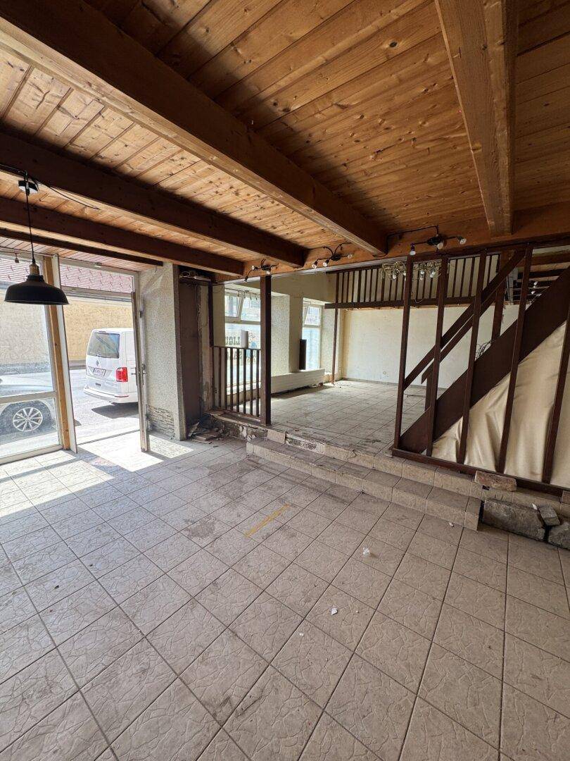 Geräumiger Innenraum mit sichtbaren Holzbalken, Fliesenboden und Zugang zur oberen Ebene.