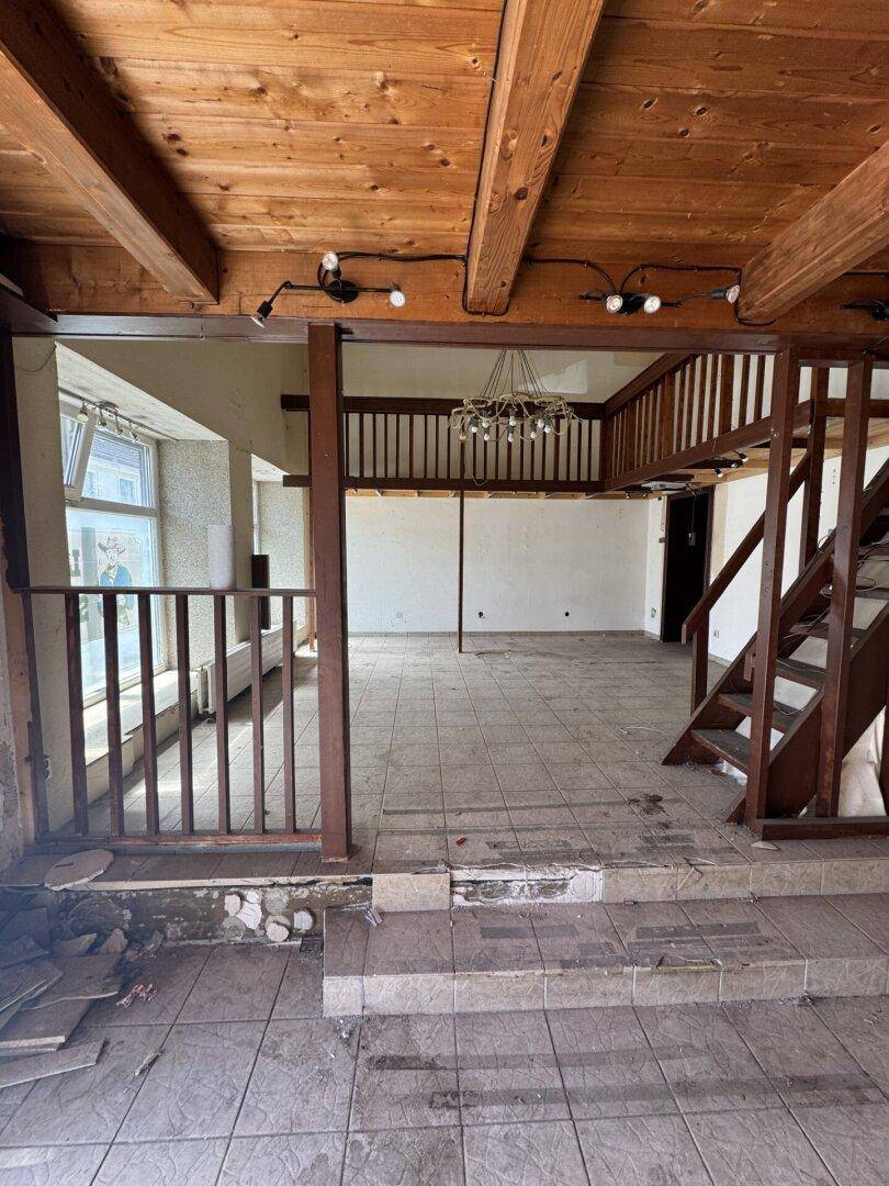 Großer, leerer Raum mit Holzbalkendecke, Fliesenboden und einer Holztreppe zur Empore.