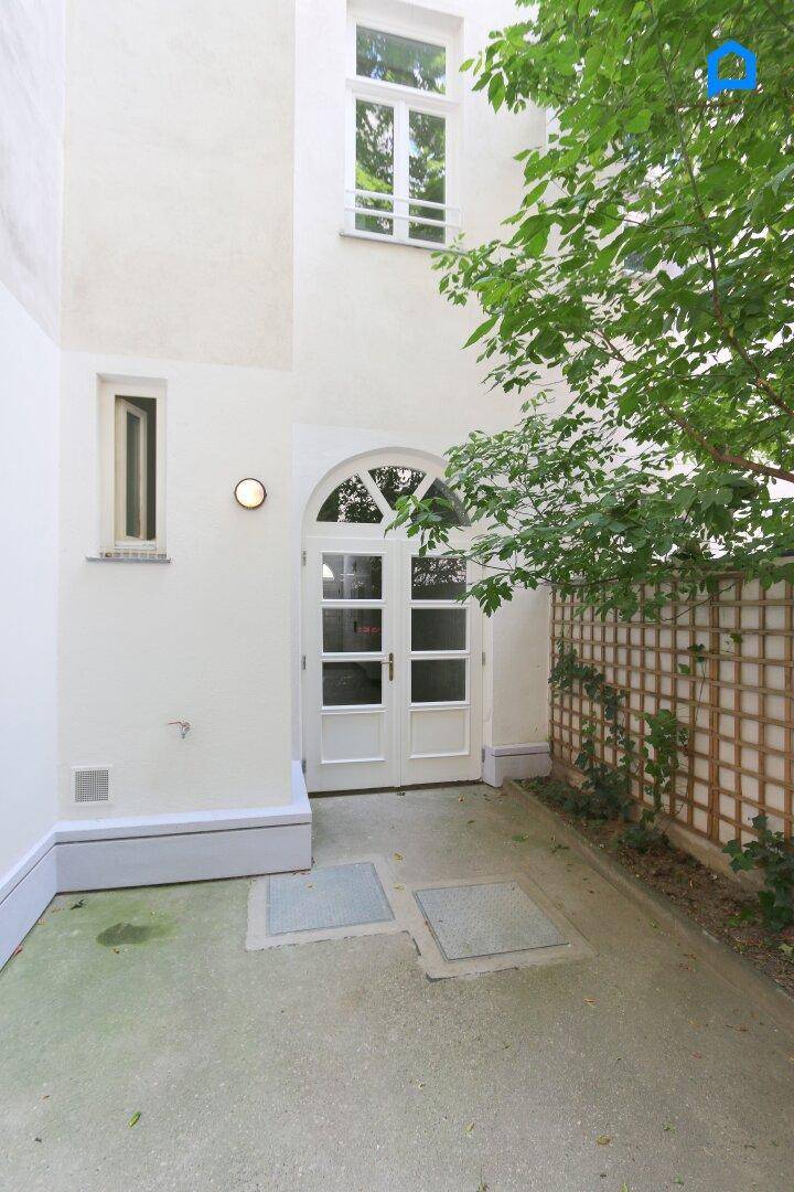 Kleiner Innenhof mit begrünten Wänden und einer gewölbten Tür, die zum Gebäude führt.