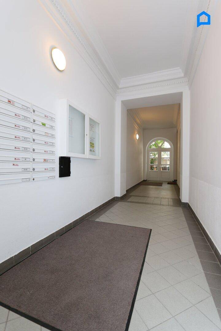 Heller Eingangsbereich mit Fliesenboden, Briefkästen und Zugang zu einem begrünten Innenhof.