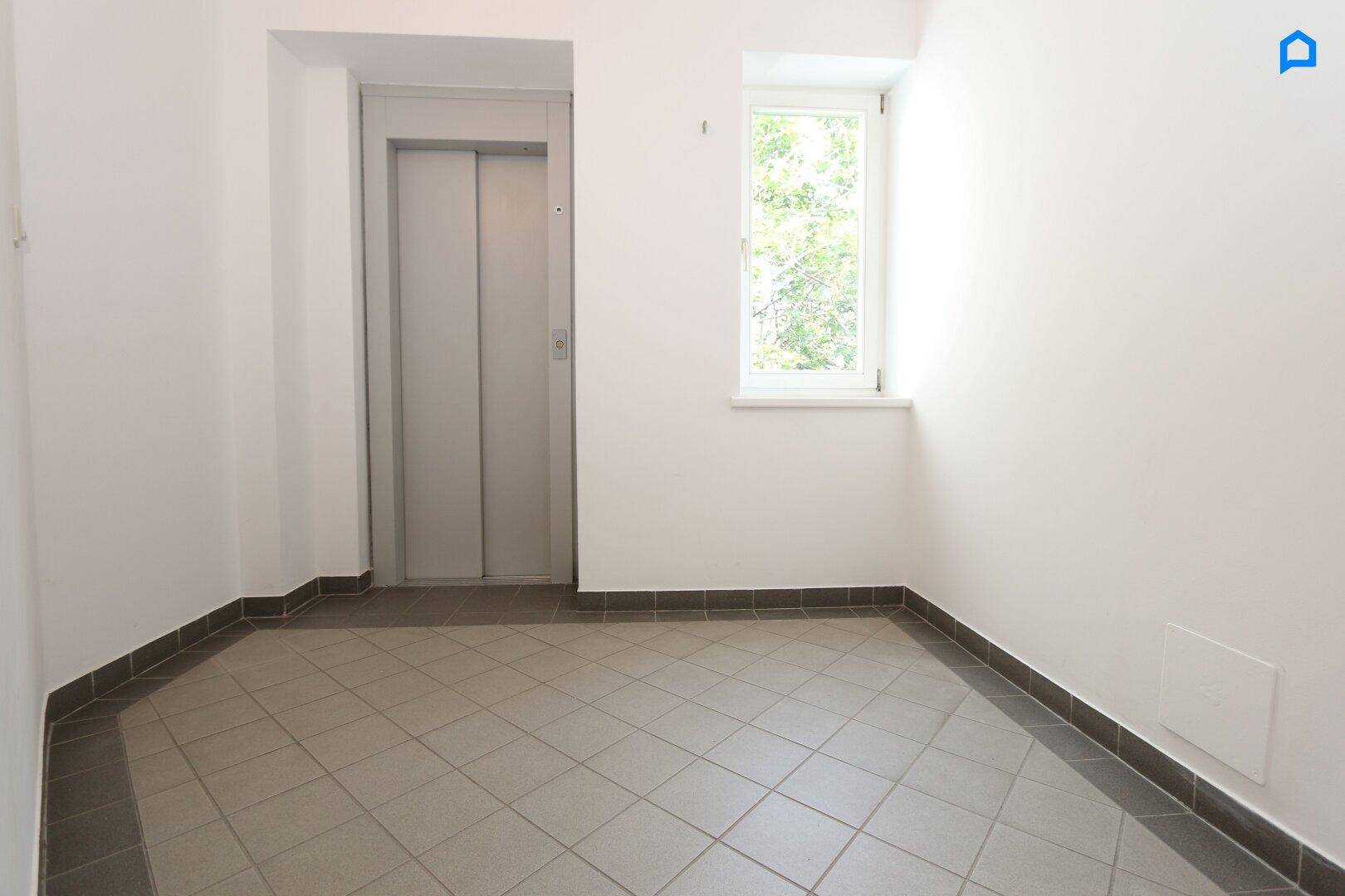 Heller Flur mit Fliesenboden und einem modernen Aufzug, der die oberen Etagen erschließt.