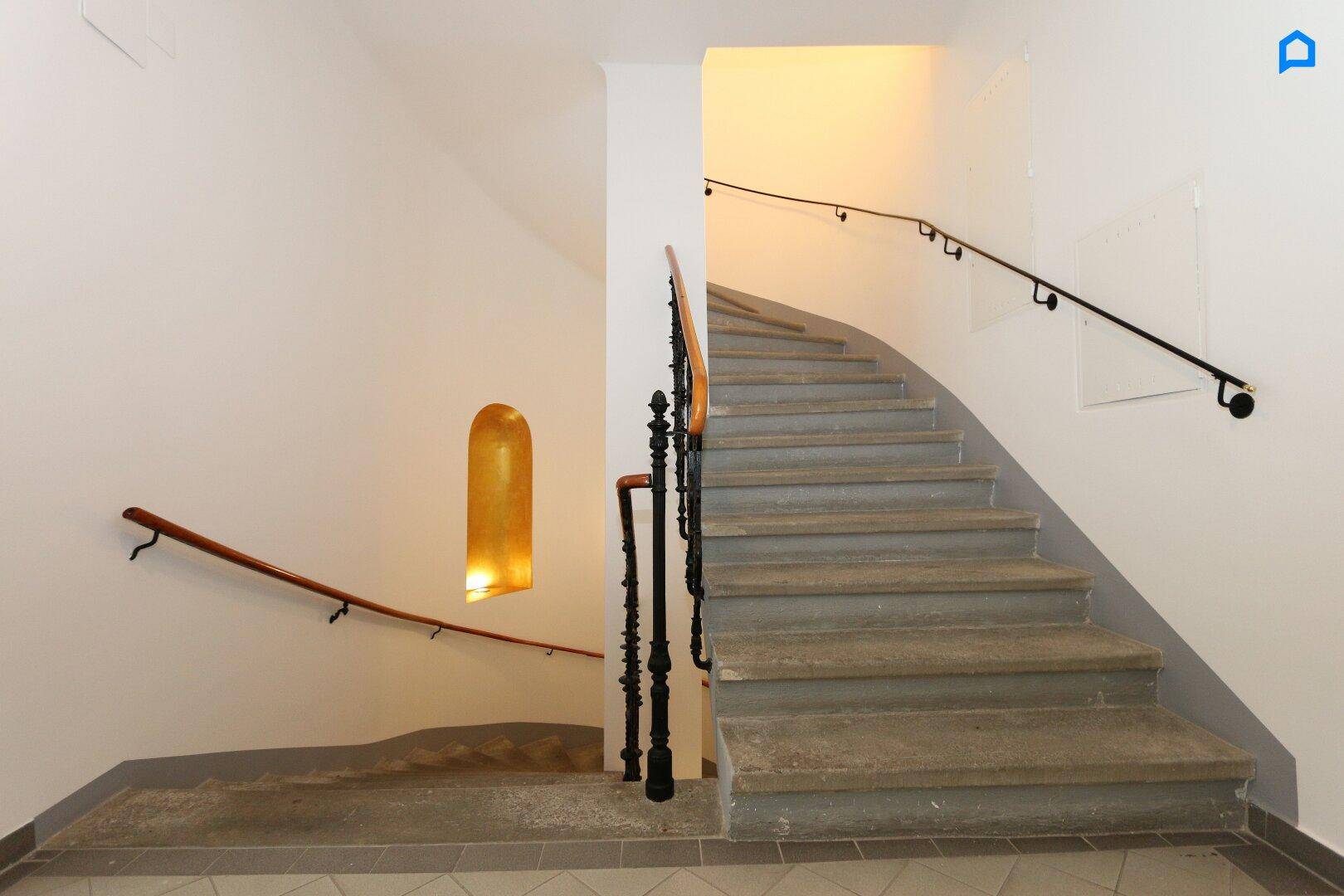 Historisches Treppenhaus mit Steinstufen und schmiedeeisernem Geländer in einem Altbau.