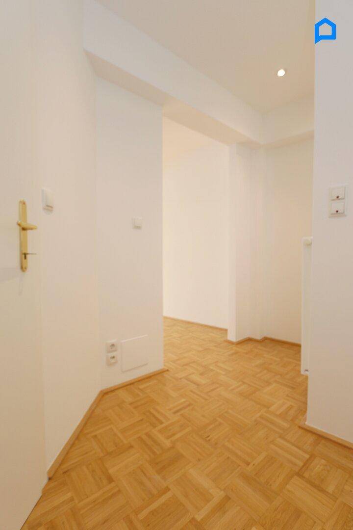 Heller Flur mit Parkettboden und weiß gestrichenen Wänden, der zu weiteren Räumen führt.