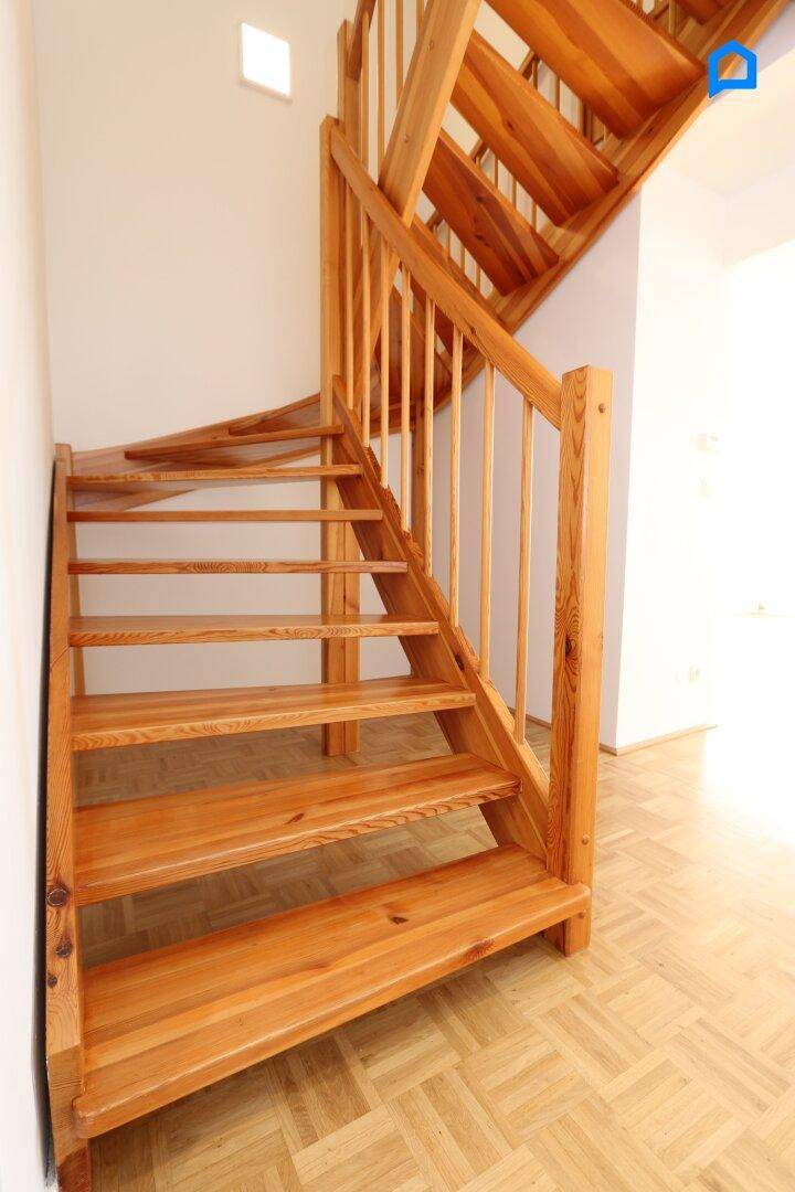 Heller Flur mit Holztreppe, die in das obere Stockwerk führt, und Parkettboden.