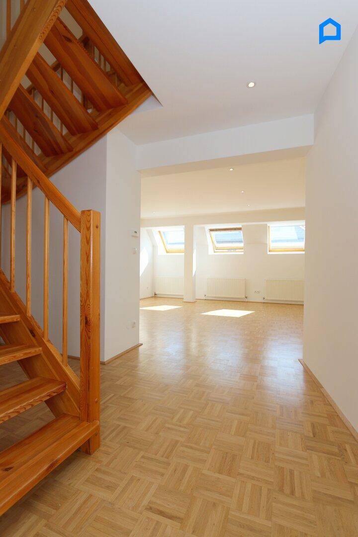 Heller Flur mit Holztreppe und Zugang zu einem lichtdurchfluteten Wohnbereich mit Parkettboden.