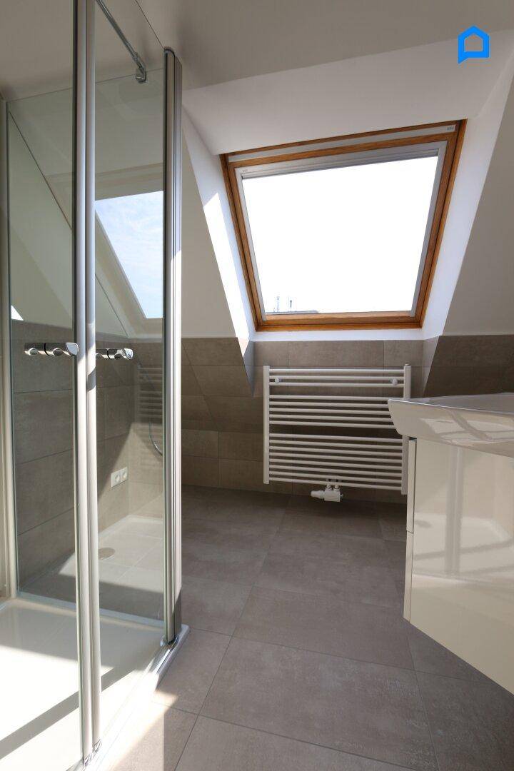 Modernes Badezimmer im Dachgeschoss mit Dusche, Heizkörper und großem Dachfenster für viel Licht.