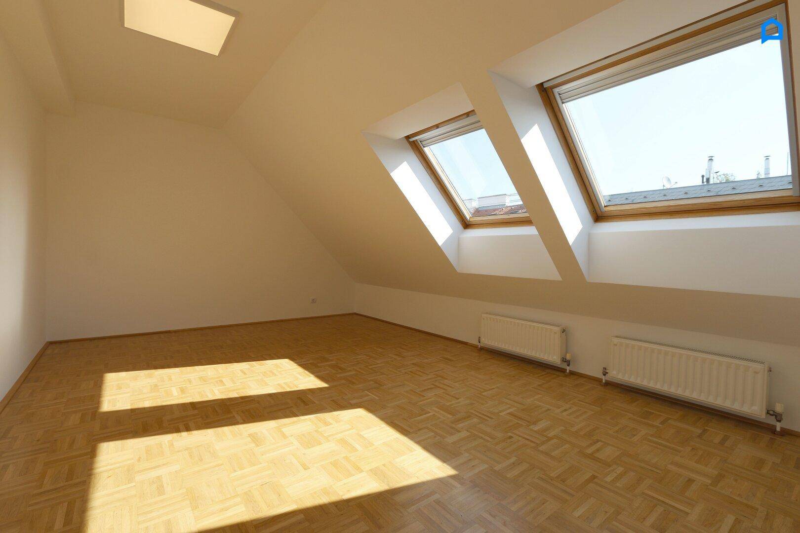 Helles Zimmer im Dachgeschoss mit Parkettboden und zwei großen Dachfenstern, die viel Licht spenden.