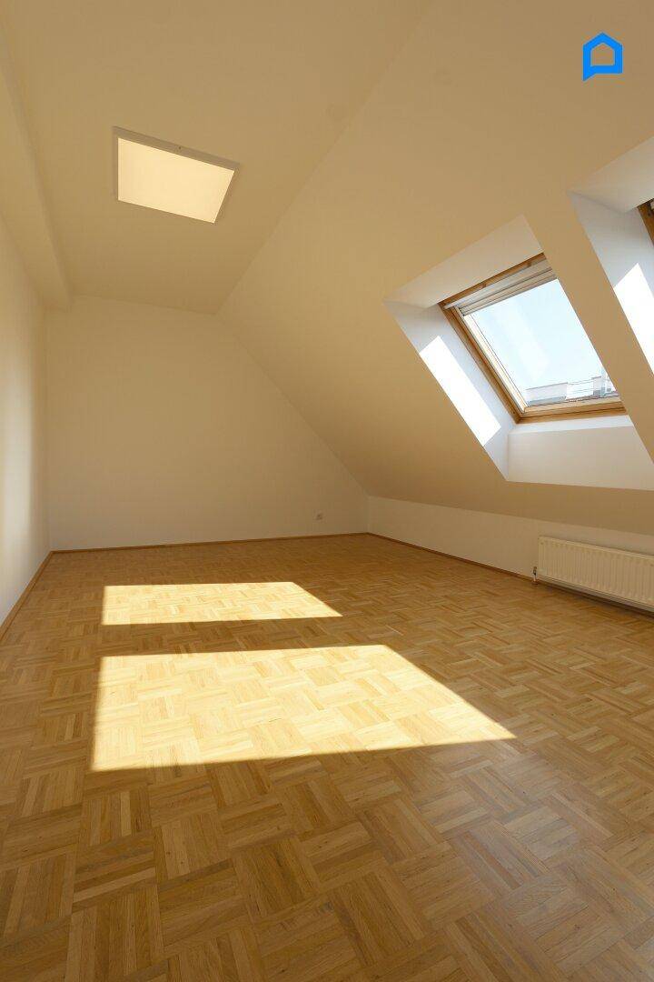 Helles Zimmer im Dachgeschoss mit Parkettboden und zwei großen Dachfenstern, die viel Licht spenden.