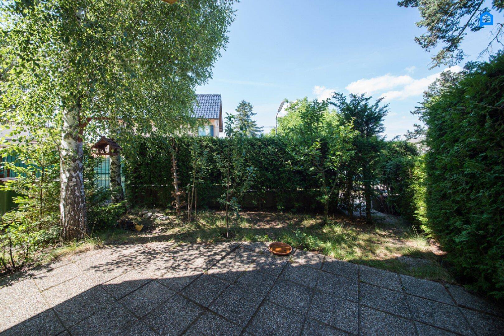 Gepflegter Garten mit Terrasse, umgeben von grünen Hecken und Bäumen.
