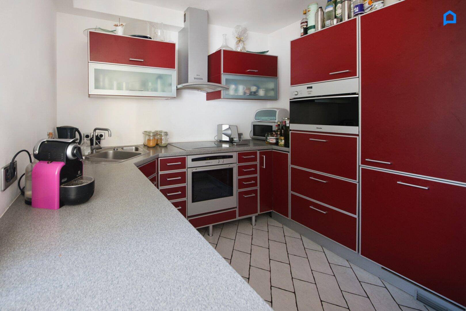 Moderne Küche mit roten Schränken, integriertem Backofen und Fliesenboden.