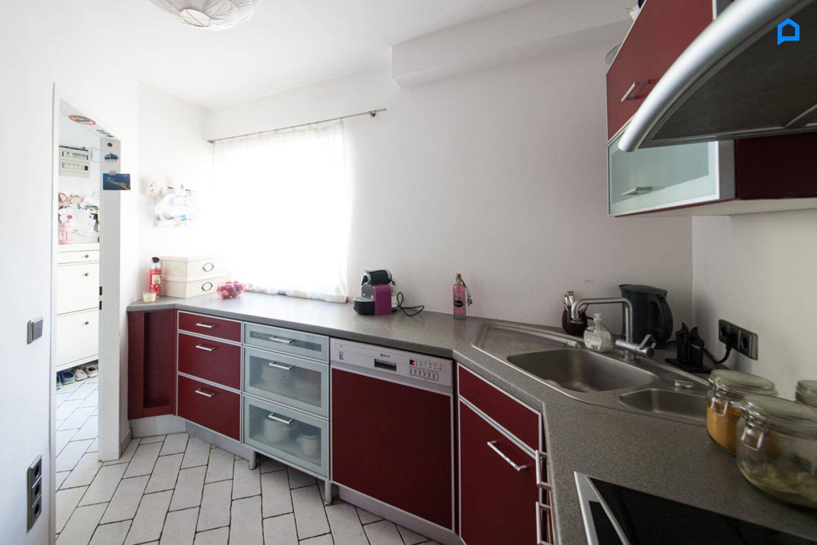 Funktionale Küche mit roten Schränken, Spülmaschine und Fenster.