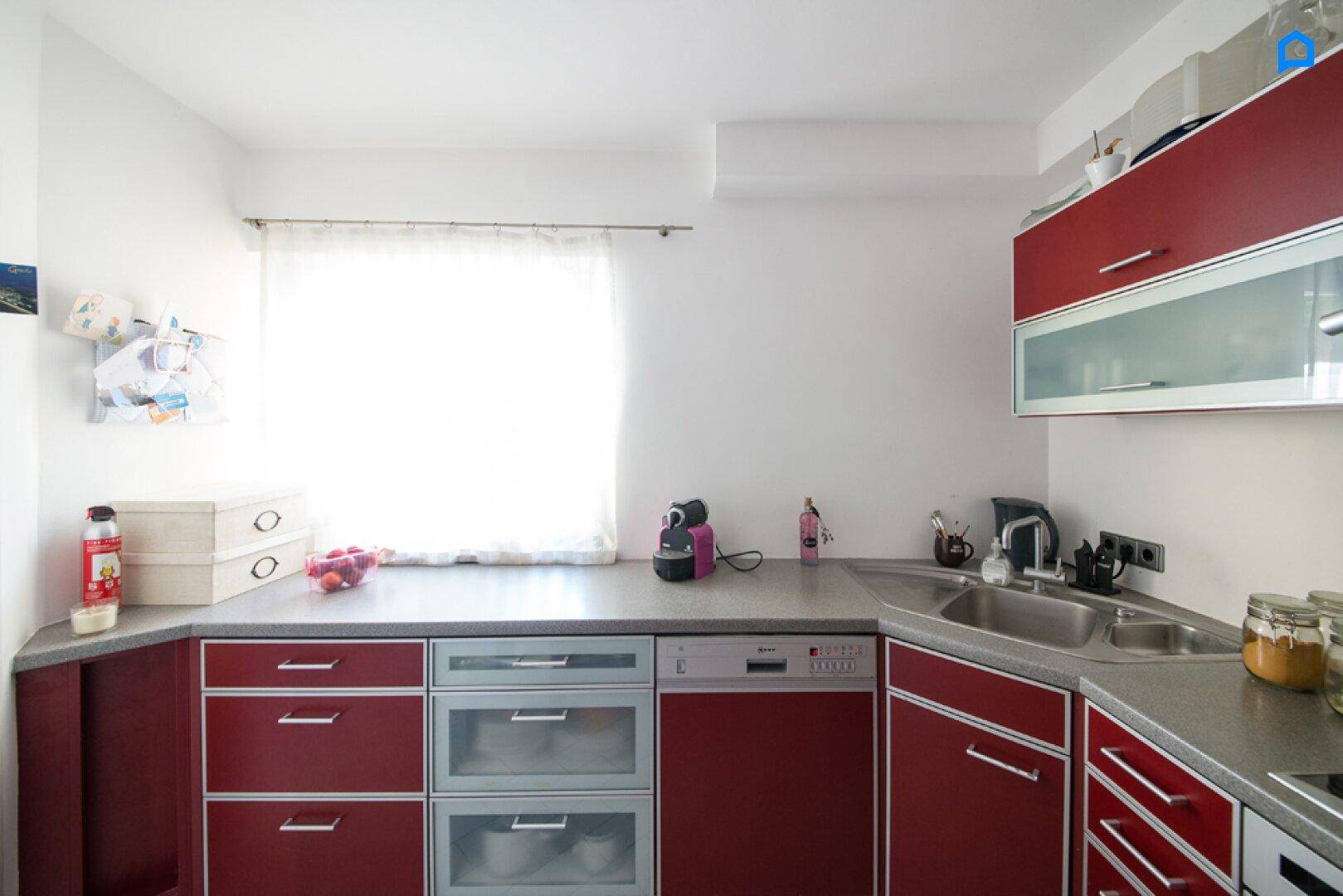 Helle Küche mit roten Unterschränken, Spülmaschine und Fenster.