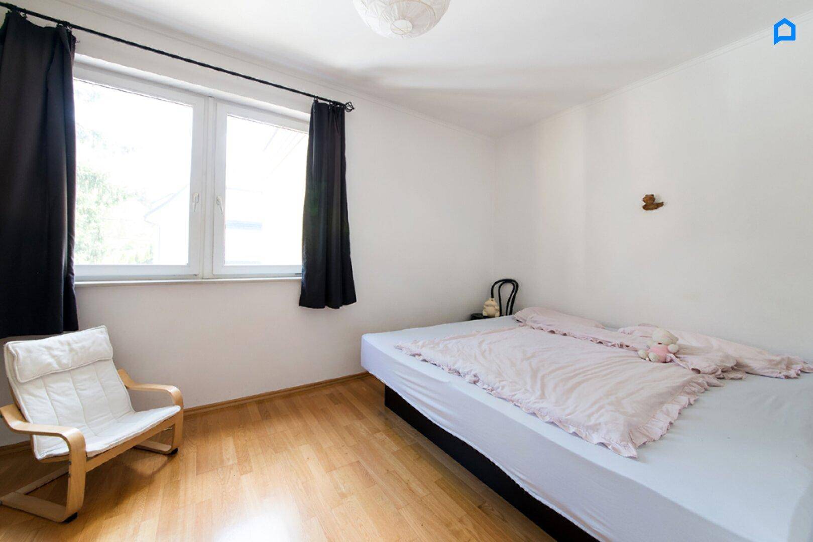 Helles Schlafzimmer mit Doppelbett, Parkettboden und großem Fenster.