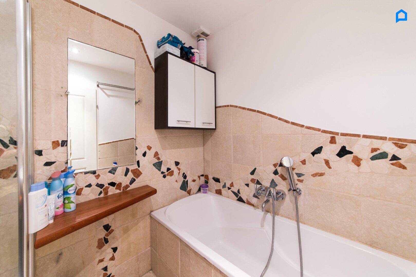 Badezimmer mit Badewanne und dekorativen Fliesen in warmen Erdtönen.