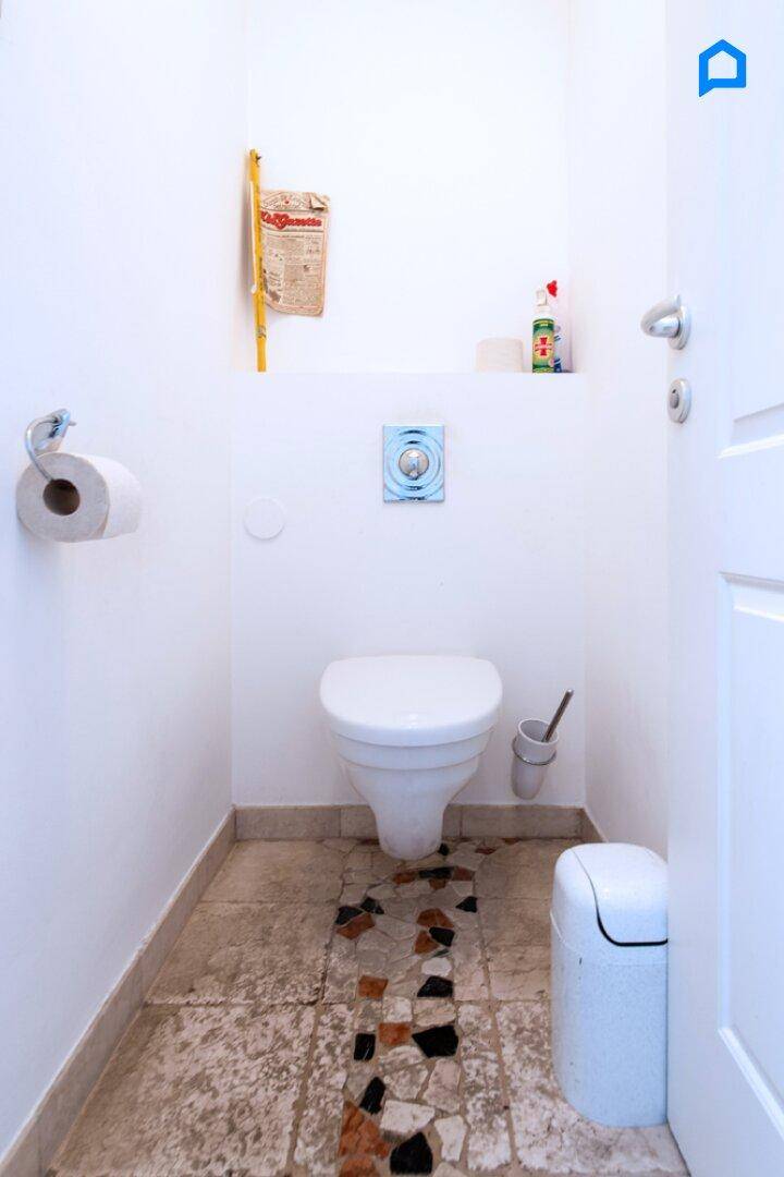 Separate Toilette mit Wand-WC und dekorativem Fliesenstreifen auf dem Boden.