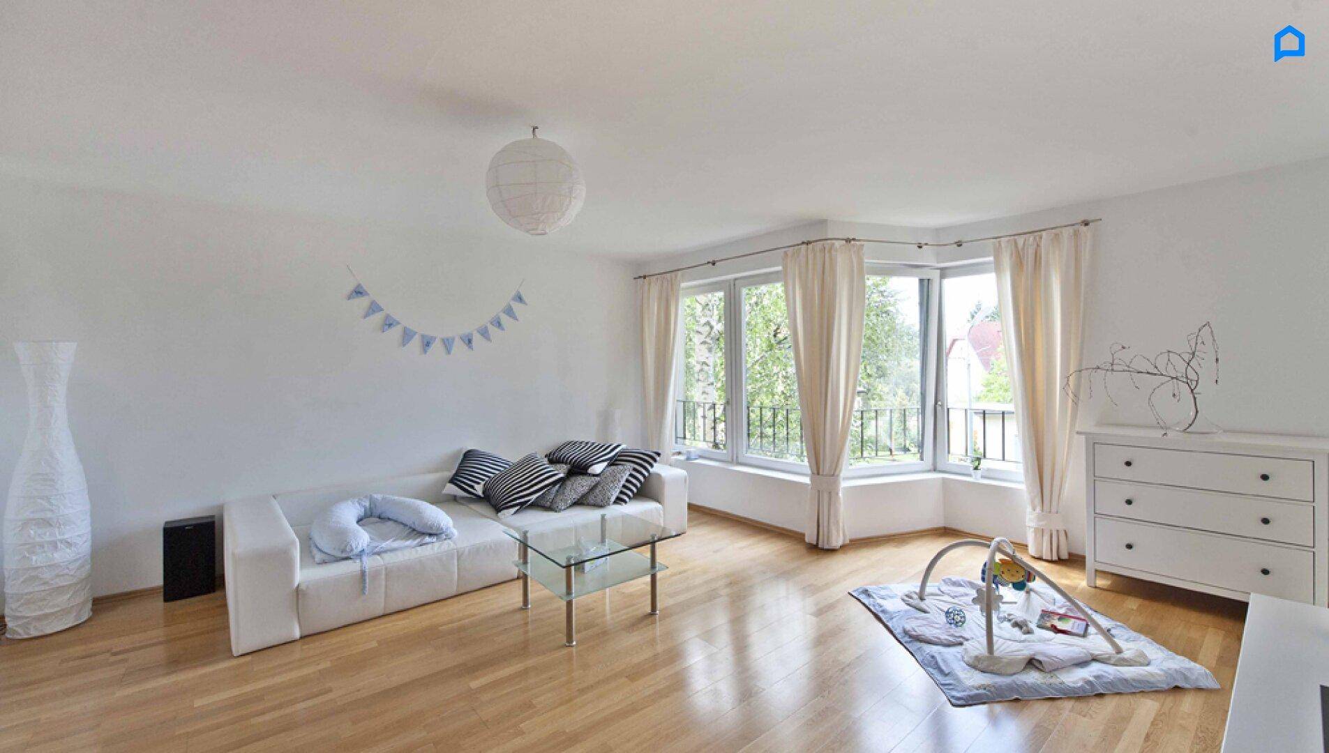 Helles Wohnzimmer mit weißem Sofa, Couchtisch und großen Fenstern.
