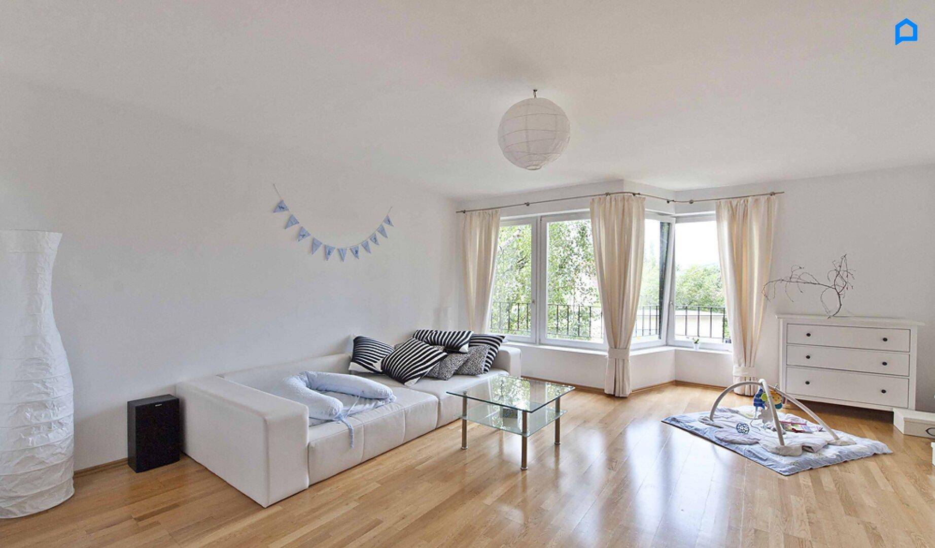 Helles Wohnzimmer mit weißem Sofa, Couchtisch und großen Fenstern.