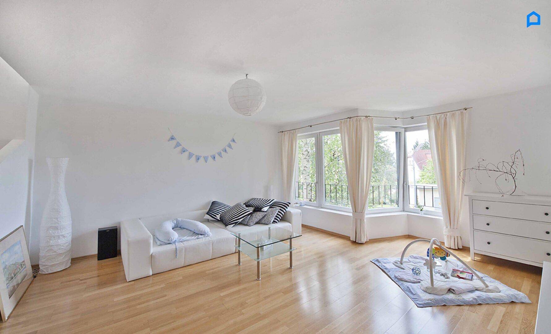 Helles Wohnzimmer mit weißem Sofa, Couchtisch und großen Fenstern.