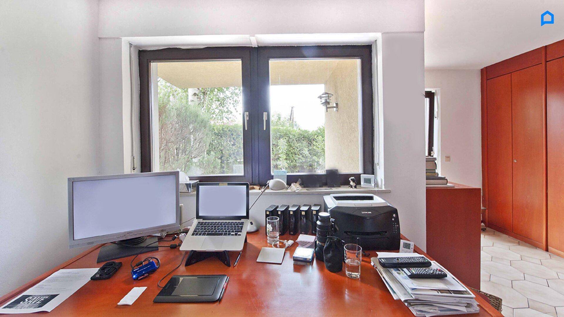 Arbeitszimmer mit großem Schreibtisch, Computern und Blick ins Grüne.