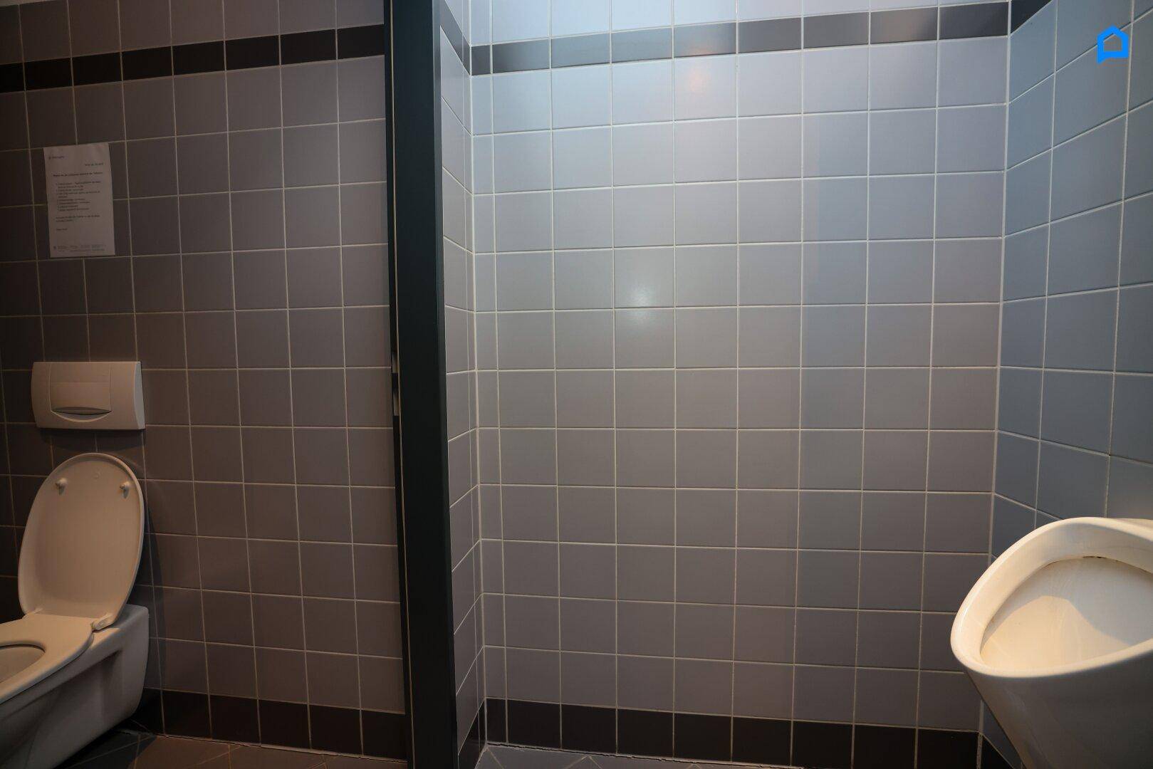 Toilettenbereich mit grauen Fliesen, ausgestattet mit Toilette und Urinal.