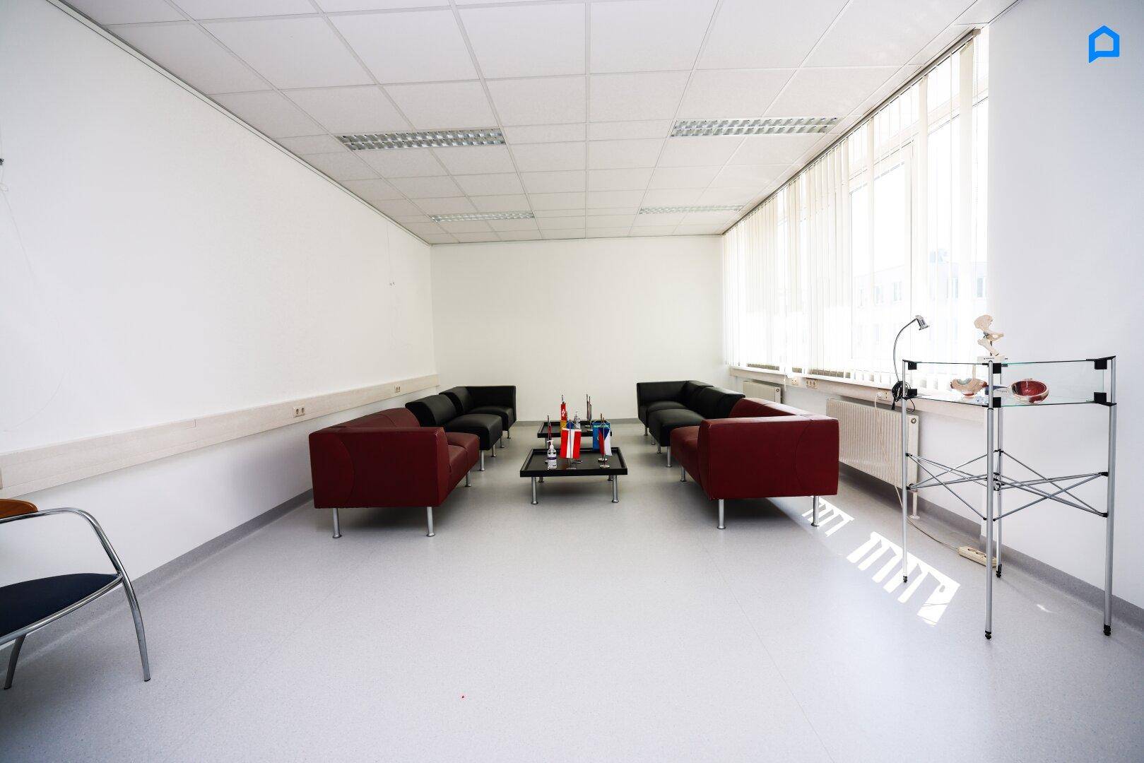 Gemütlicher Loungebereich mit roten und schwarzen Sofas, Couchtischen und großen Fenstern.