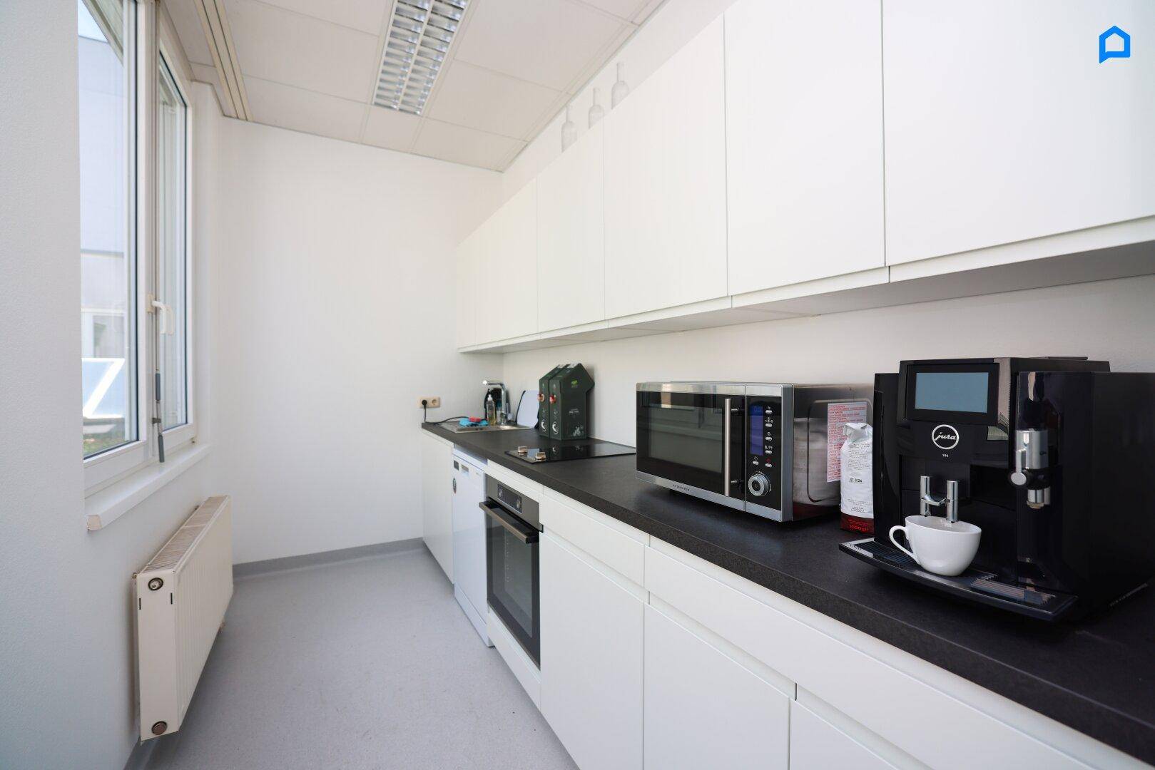 Detailansicht der Teeküche mit Mikrowelle, Kaffeemaschine und integriertem Backofen.