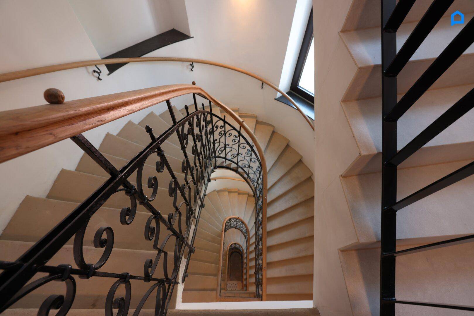 Wendeltreppe mit kunstvollem schmiedeeisernem Geländer und Holzhandlauf in einem historischen Gebäude.