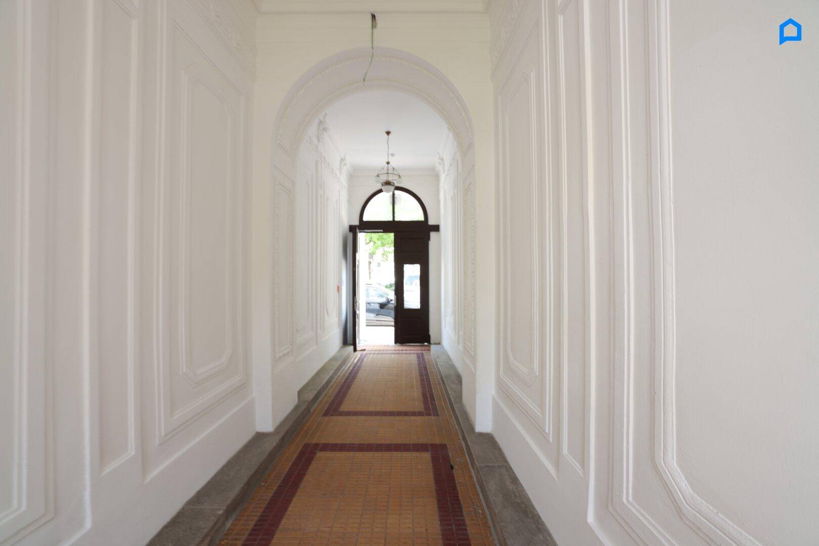 Langer, heller Flur mit eleganten Wandpaneelen und einem Bogenportal zum Eingangsbereich.