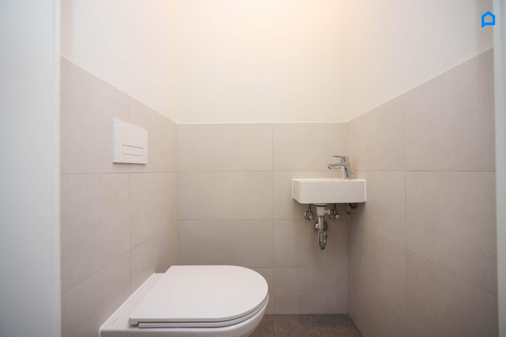 Modernes Gäste-WC mit wandhängender Toilette und kleinem Handwaschbecken, hell gefliest.